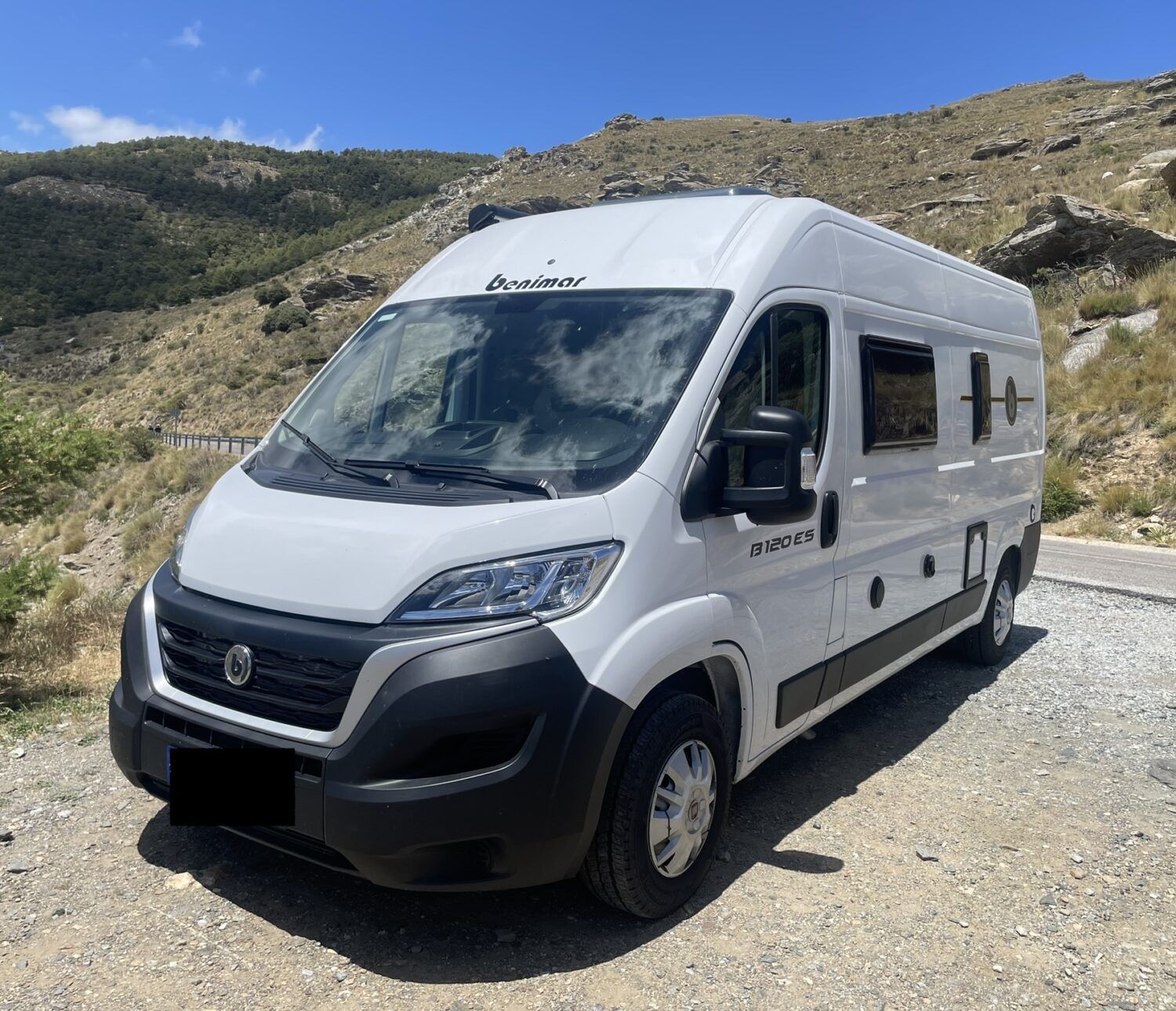 Furgoneta camper Benimar 120 ES blanca estacionada junto a la costa, ideal para recorrer España desde Alicante